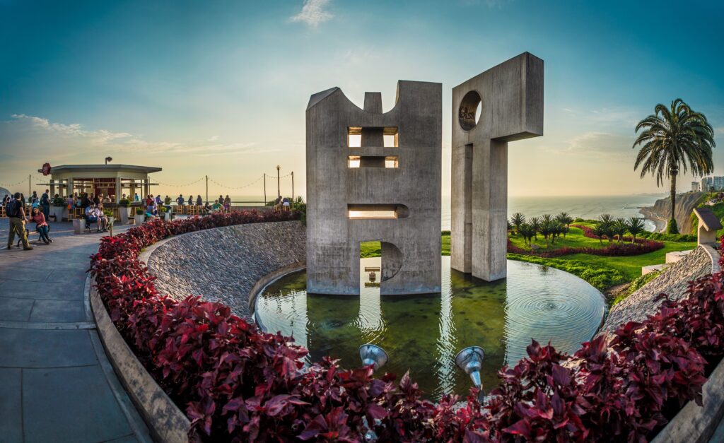 Modern concrete sculpture by the ocean in Lima, Peru with vibrant foliage and people enjoying the scene.