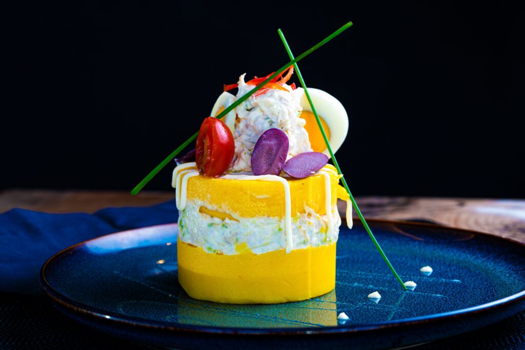 Delicious Causa Rellena beautifully plated with vibrant garnishes on a blue dish.